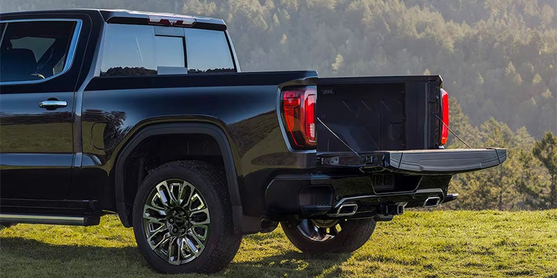 Rear side view of a black GMC Sierra Denali pickup truck parked on grass